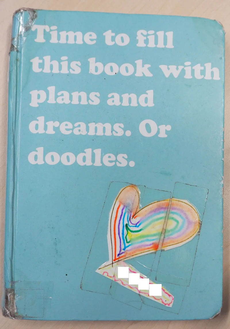 Zuzenna's aphasia diary — a teal notebook with a hand-drawn rainbow heart sticker